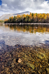Mountain lake Froliha, pine tree and stones with snow at mirror lake