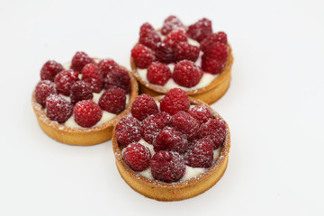 Three tartlets with raspberry on white background