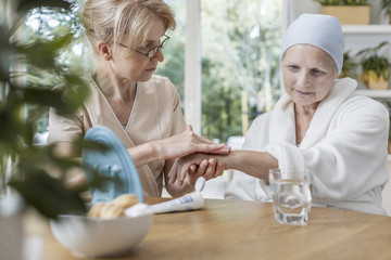 Nurse helping sick elderly woman with cancer during treatment at home