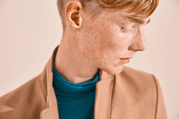 Close-up portrait of young man with red hair and freckles. Dressed in turquoise throat sweater and...