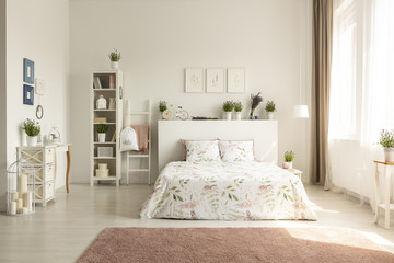 Posters above bedhead with plants in spacious bedroom interior with bed and pink carpet. Real photo