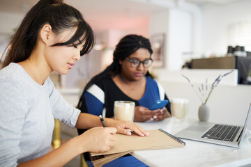 Two female students sitting by table in cafe