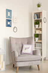 Grey armchair with pillow in bright living room interior with posters and shelves. Real photo