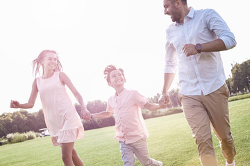 Naklejka na ściany i meble Family walk. Family of three running on grassy field smiling hap