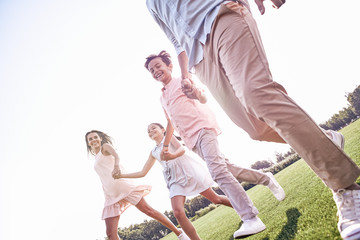 Bonding. Family of four running on grassy field laughing cheerfu