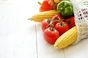 Bunch of mixed organic fruit, vegetables & greens: corn cob, tomato, pepper, lettuce salad, grapes & apples in reusable cotton net bag. Zero waste concept. Wood table background, copy space, close up.