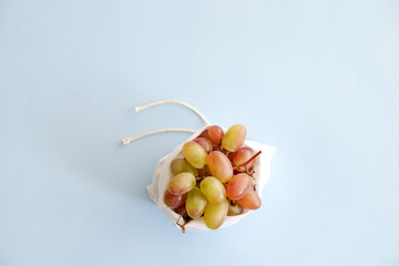 Reusable eco friendly tied cotton fabric bag stuffed with bunch of sweet organic grape branches on light blue background. Zero waste concept. Top view, close up, copy space.