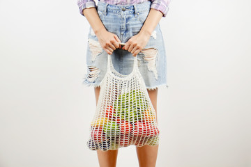 Young woman in plaid shirt, jeans skirt with bag of mixed fruit, vegetables & greens: corn cob,...