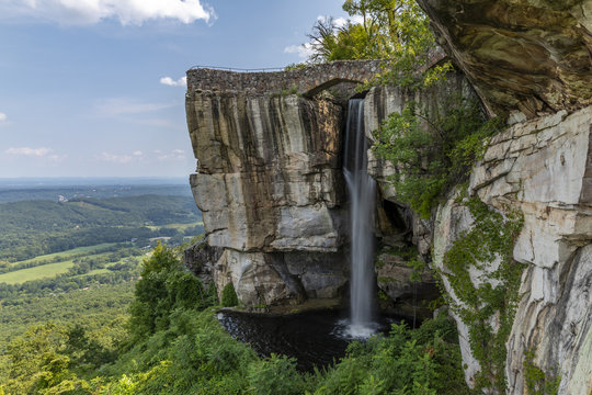 Fototapeta High Falls Waterfall - A waterfall under a footbridge on the side of a cliff.