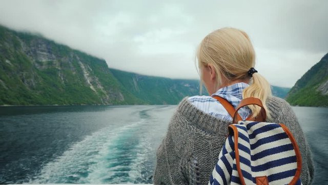 A woman stands at the stern of a cruise ship, looks at the retreating rocks and waves of the fjord