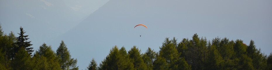 Banner, Paragleiter gleitet über die Baumgipfel ins Tal