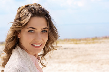 Fototapeta na wymiar portrait of smiling woman looking at camera on sandy beach