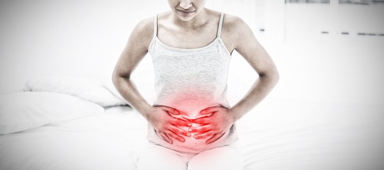 Composite image of casual woman with stomach pain sitting in bed