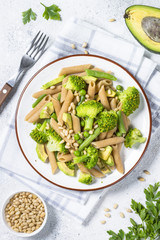Vegan pasta penne with broccoli, avocado and pine nuts top view.