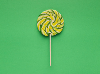 Spiral candy lollipop on green background, top view
