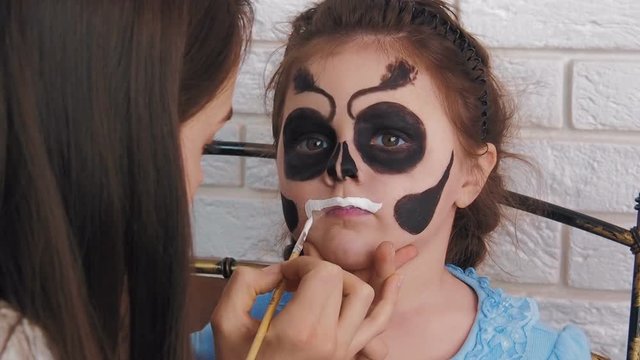 Skeleton painted on the face for Halloween. The girl is painted face for halloween.