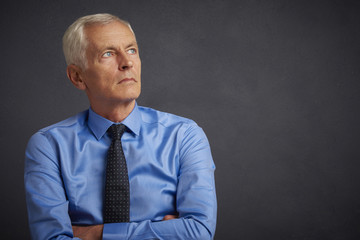 Senior man portrait. Shot of an elderly businessman wearing suit and looking up while standing at grey background. 
