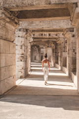 A girl in a black and white dress walks in the Arles amphitheater, creating a play of light and shadow in the arena