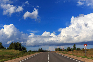 Road up hill with green grass field under white clouds and blue sky in summer day. Latgale. Latvia
