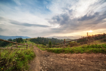 Fototapeta na wymiar old wooden fence, rural road and top of mountain on horizon on sunset. summer (autumn) landscape