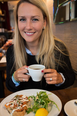 Smiling Beautiful Young Woman Holding a Coffee Cub at Lunch in a Restaurant