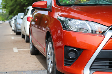 Fototapeta premium Closeup of front side of modern red car park in parking area beside the street in sunny day.