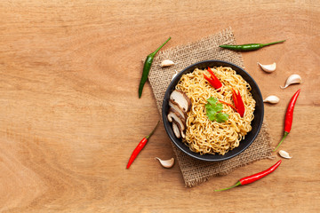 Instant noodles in the bowl with pepper and garlic on brown wooden background. Top view and Copy space