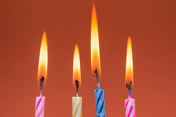 Burning birthday candles close up macro shot on dark red background.