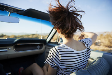 Rear View Of Female Passenger On Road Trip In Classic Convertible Car 