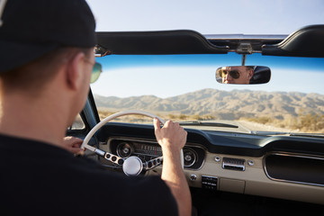 Rear View Of Man On Road Trip Driving Classic Convertible Car Towards Sunset