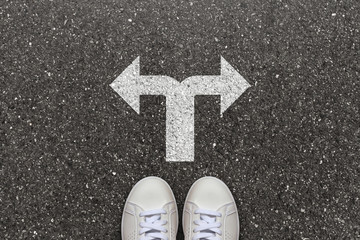 Fototapeta premium White sneakers on a asphalt road with choice arrows and thinking about it. Decision making and choices concept