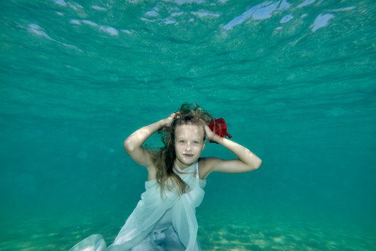 Young woman with long hair underwater portrait in white dress with red flower. Mermaid concept.