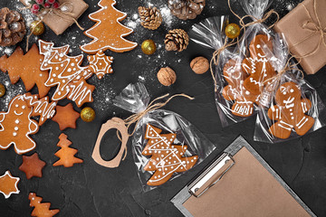 A Christmas gingerbread cookie in the shape of a Christmas tree in a cellophane packing on the background of a dark table. Christmas gift concept. - obrazy, fototapety, plakaty