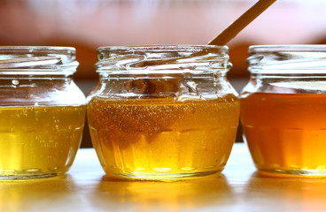three cans of honey of different colors with a wooden spoon