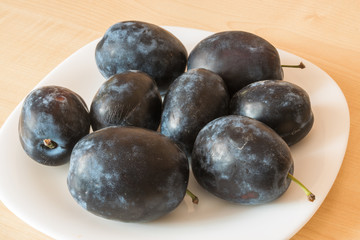 Plum fruits on the plate on the table.