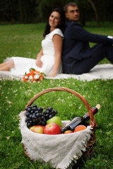 Basket with products for a picnic on the clearing, in the distance newlyweds