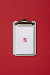 Clipboard home made by, on red background. Flat lay, top view trendy for banner