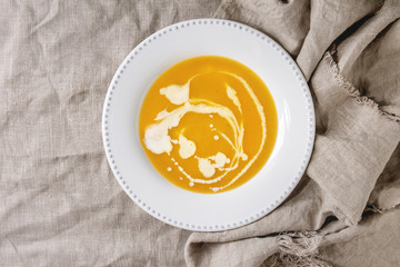 Plate of vegetarian pumpkin carrot soup decorated by cream spots over linen cloth as background. Flat lay, copy space