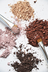 different colors piles of eyeshadows with brushes on white background 