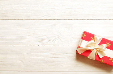 Christmas and new year present wrapped in festive colorful red and white paper, yellow silk bow. Single holiday gift box on white wooden texture table. Close up, background, copy space, top view.
