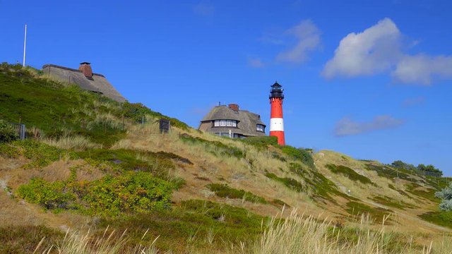 Leuchtturm H&ouml;rnum Sylt mit D&uuml;nen Landschaft  Reetdach H&auml;usern und  blauen Himmel

