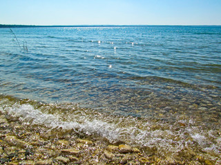 Transparent water and pebbles on the beach coast. Summer coastline landscape on sunny day on Lake Michigan, North America.