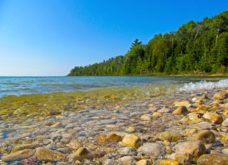 Transparent water and pebbles on the beach coast. Summer coastline landscape on sunny day on Lake Michigan, North America.