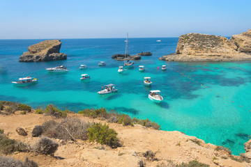 Boats anchored in small cove Blue lagoon on Comino island in Malta. Turquoise sea, azure ocean, yachts and sailing boats. Panorama view on bay with crytal clear water. - obrazy, fototapety, plakaty