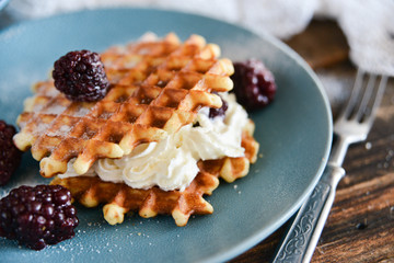 Round waffles with fresh blackberries and whipped cream, on natural wooden background in rustic style