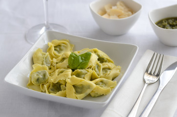 Italian ravioli filled with ricotta cheese and spinach decorated with basil, served with parmesan and pesto. Restaurant pasta dish background.