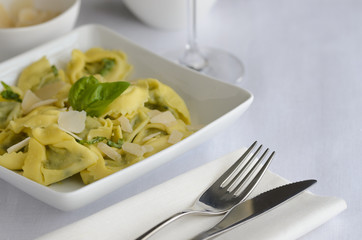 Italian ravioli filled with ricotta cheese and spinach decorated with basil, served with parmesan and pesto. Restaurant pasta dish background.