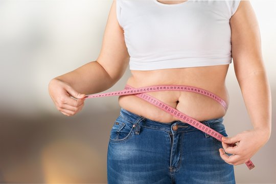 Overweight, fat woman measuring her stomach on background