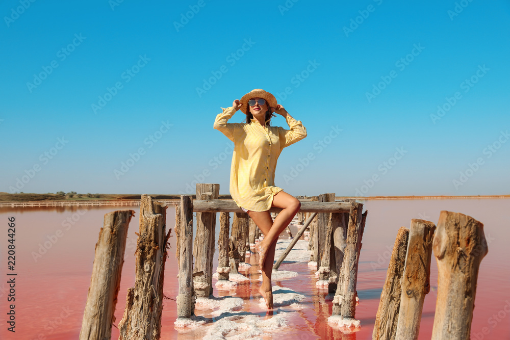 Wall mural Beautiful woman with hat posing near pink lake on summer day