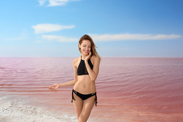 Fototapeta na wymiar Beautiful woman in swimsuit posing near pink lake on sunny day